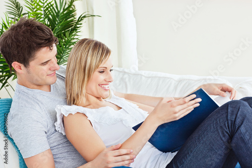 Cute couple browsing a book lying on the sofa