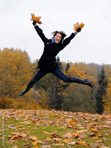 beautiful girl with autumn leafs in a park jumping and smiling