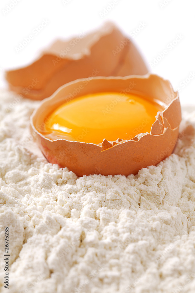 Broken egg with shells on flour, white backdrop