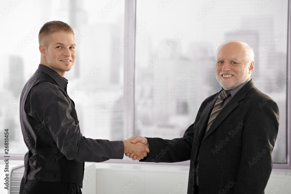 Senior executive shaking hands with young employee Senior executive shaking hands with young employee