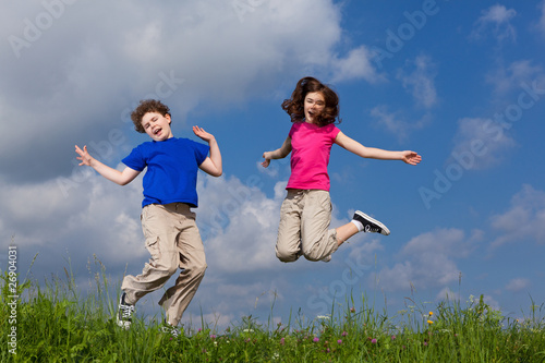 Girl and boy jumping, running against blue sky