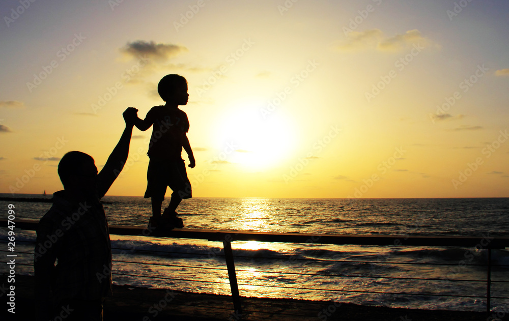 silhouettes of father and son on sunset sea background