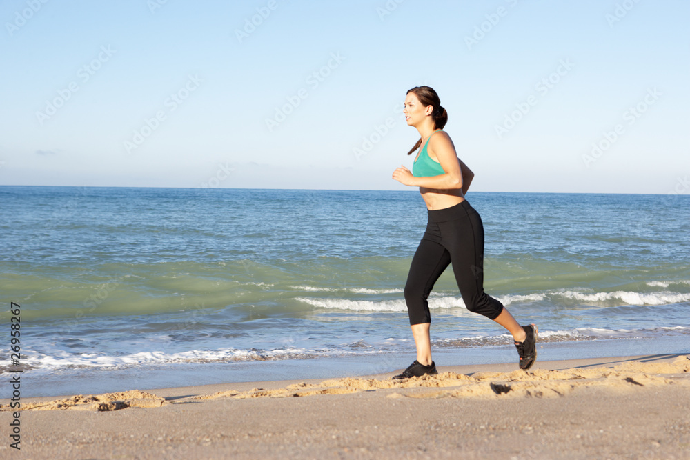 Young Woman In Fitness Clothing Running Along Beach Young Woman In Fitness Clothing Running Along Beach