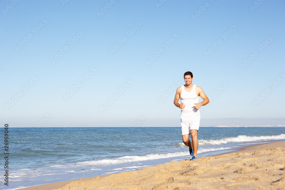 Young Man In Fitness Clothing Running Along Beach Young Man In Fitness Clothing Running Along Beach