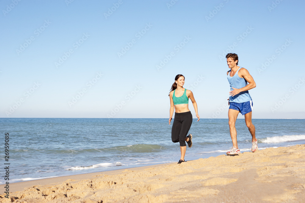 Young Couple In Fitness Clothing Running Along Beach Young Couple In Fitness Clothing Running Along Beach
