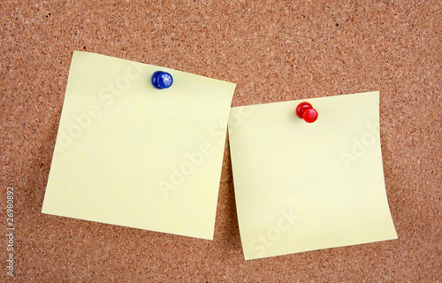 two yellow memo sticks with pins on cork board