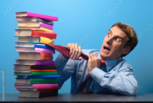 man at the table looking with fear at a stack of colored books