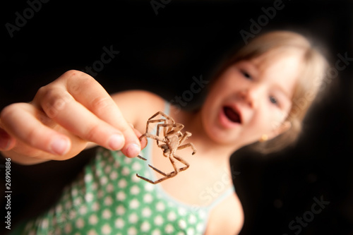 young girl holding a brown spider by leg and surprised