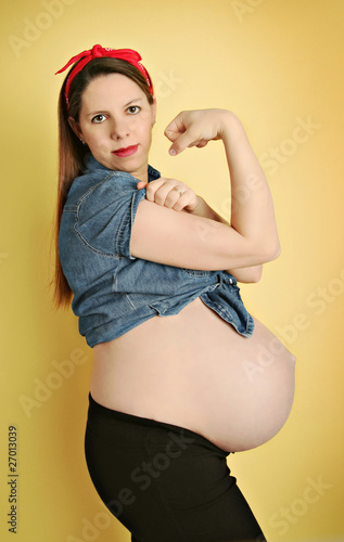 Young pregnant woman showing belly and flexed arm muscles