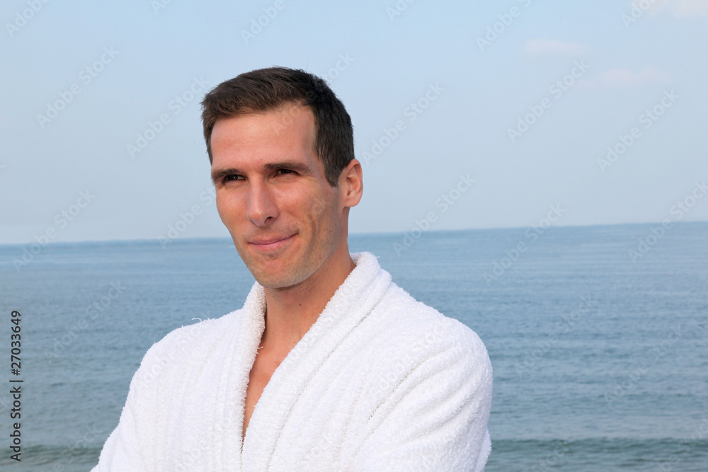 Smiling man standing by the sea in bathrobe