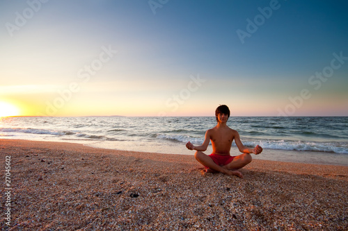 Teen boy at the beach meditating on sunset