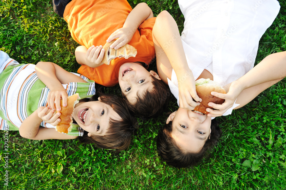 Fototapeta premium Three children laying on grass on ground, eating