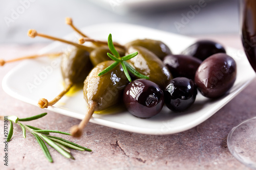 Caper berries and black olives on a stone background