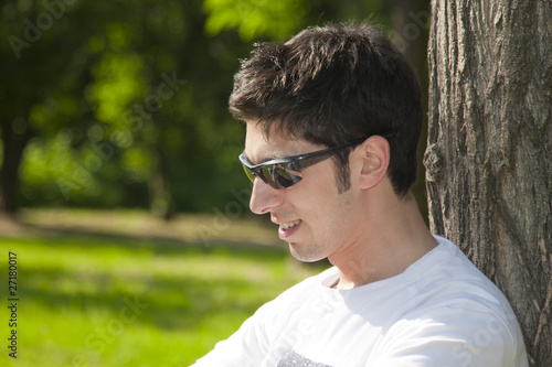 Young man relaxing upon a tree in the park