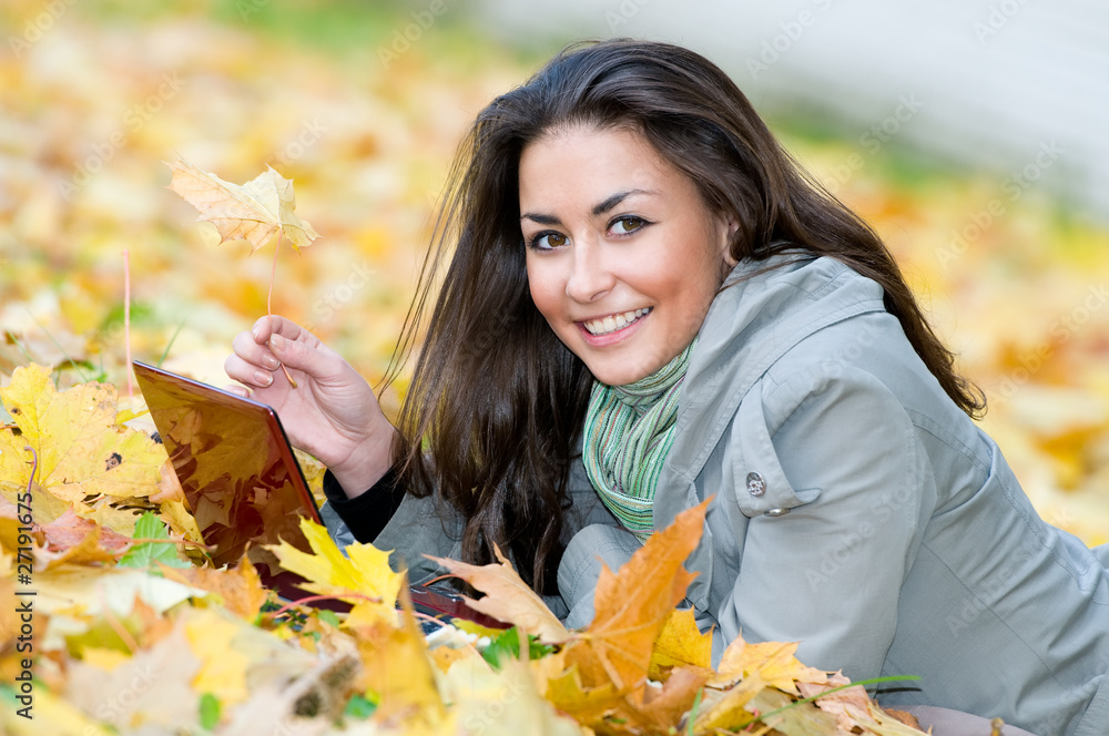 Happy student girl lying in autumn leaves with netbook Happy student girl lying in autumn leaves with netbook