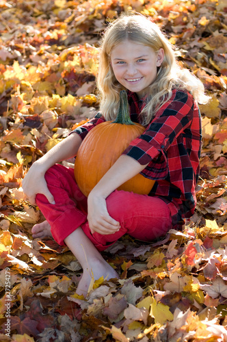 young girl with pumpkin on bed of fall leaves