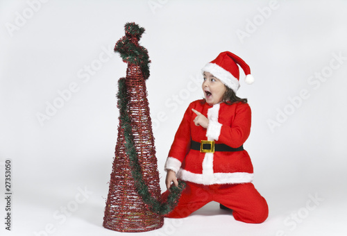 niña vestida de papa noel señalando arbol de navidad photo