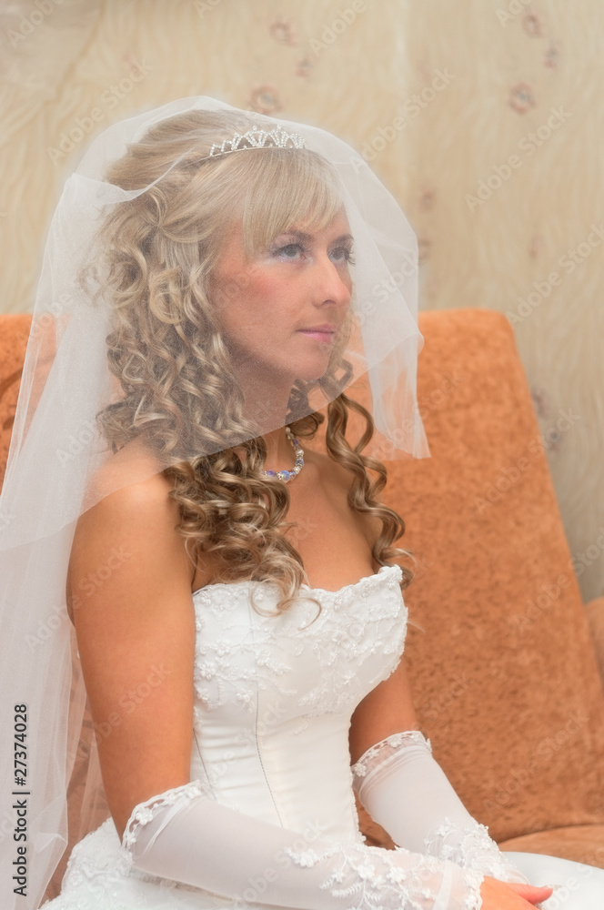 Bride young blonde girl sitting on couch with veil on her face Bride young blonde girl sitting on couch with veil on her face
