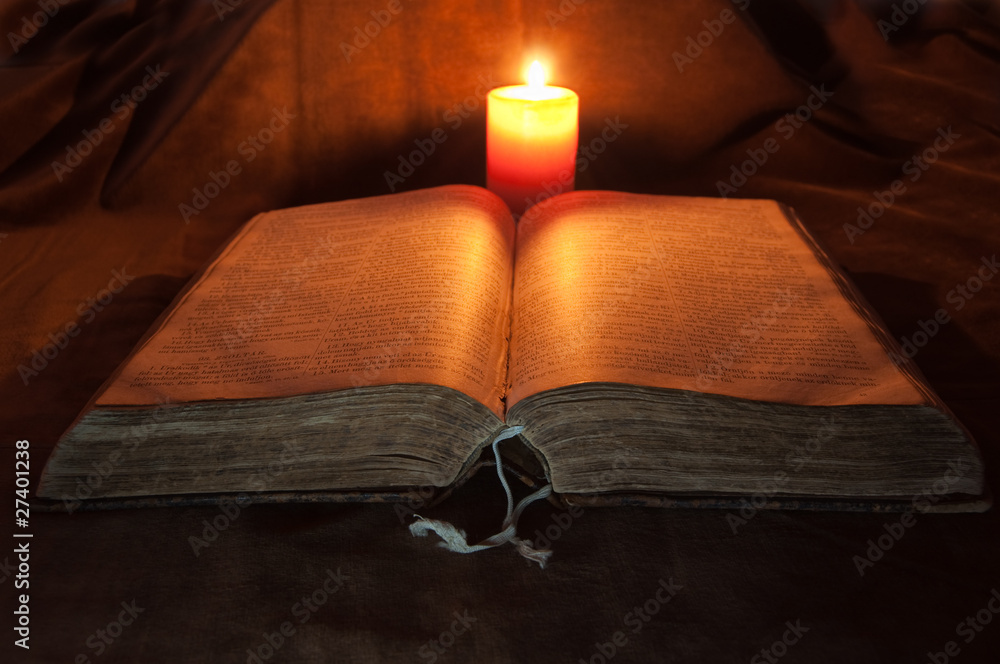 Naklejka premium Bible lighted by a Candle