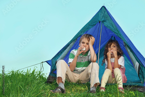 Small children have rest on nature, sit near tent and eat