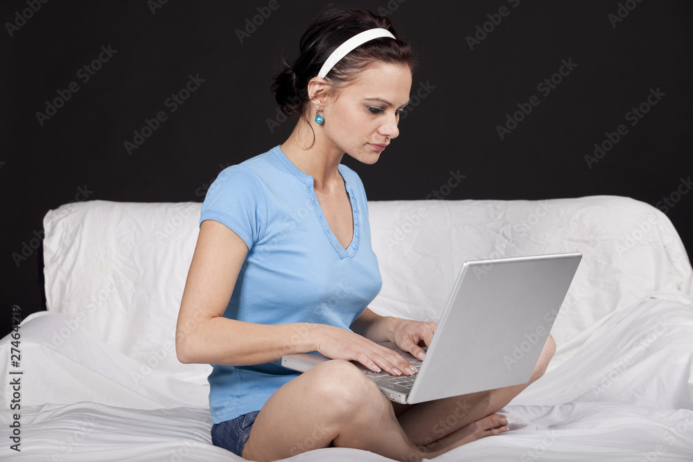 Pretty young woman sitting on bed with her laptop Pretty young woman sitting on bed with her laptop
