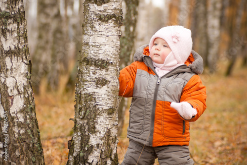 young cheerful baby touching tree in autumn forest park