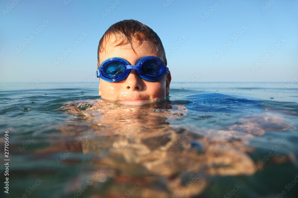 Naklejka premium boy in spectacles for swimming swims in sea. blue sky