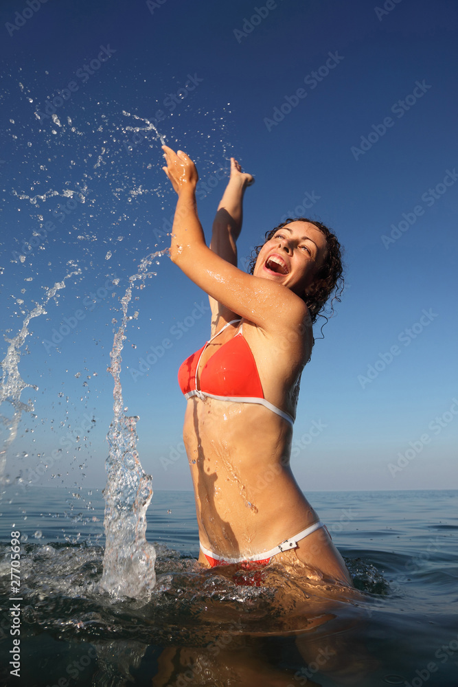 woman wearing red bathing suit spinning in sea. many drops