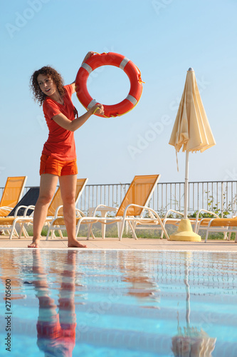 young woman in shorts and T-shirt throws red buoy ring to pool