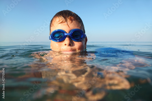 boy in spectacles for swimming swims in sea. blue sky © Pavel Losevsky