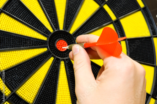 Male hand throwing dart arrow in bulls eye on dart board game photo