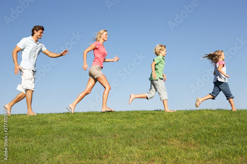 Young family, parents with children, running through field