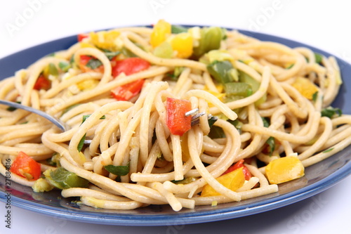 Spaghetti with vegetables being eaten with a fork on white