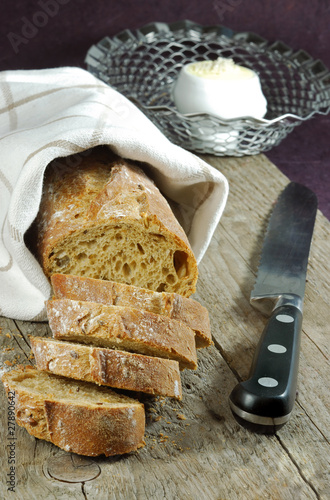 A sliced french baguette on a wooden board with bread knife