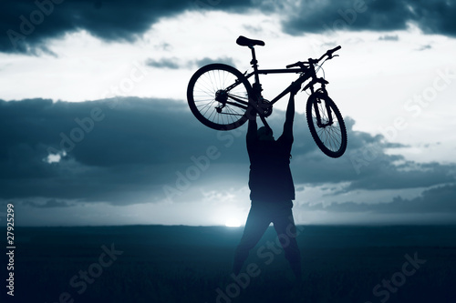 Fototapeta Naklejka Na Ścianę i Meble -  Man holding a bicycle over himself on sunset background