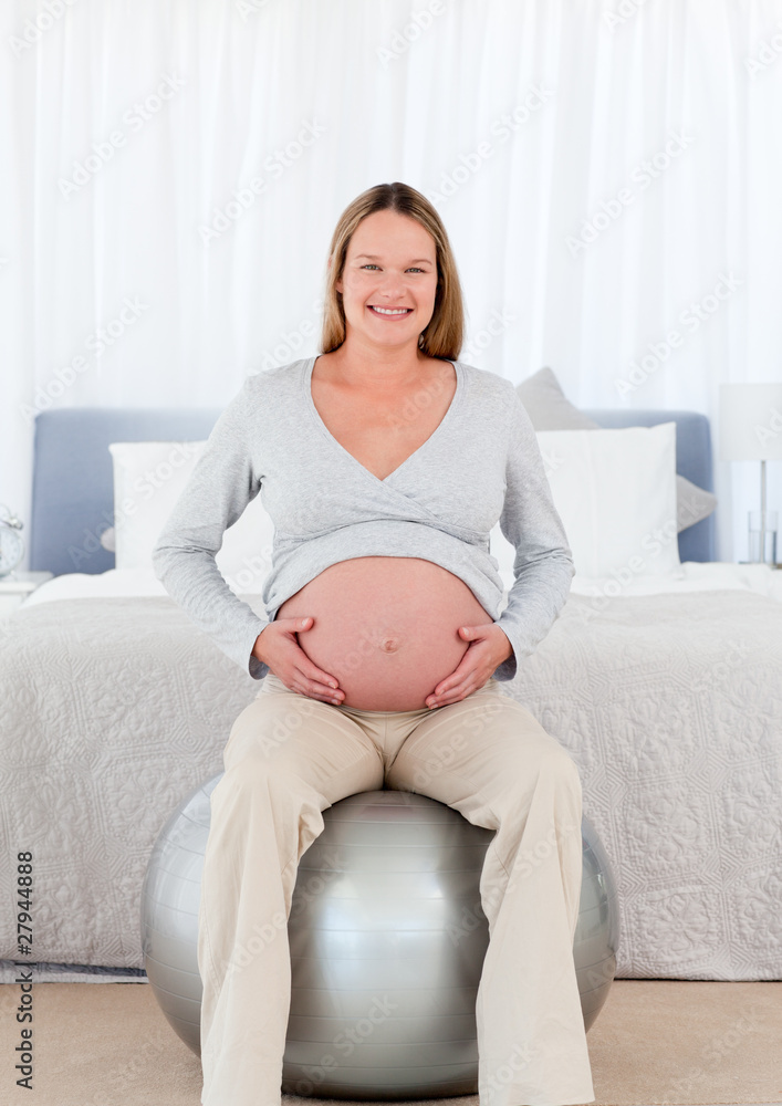 Pretty future mother sitting on a fitness ball and touching her Pretty future mother sitting on a fitness ball and touching her
