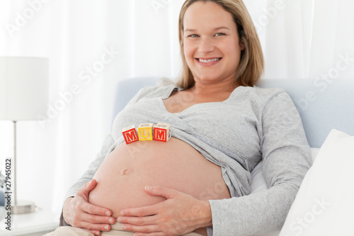 Joyful pregnant woman with mom letters on her belly while relaxi photo