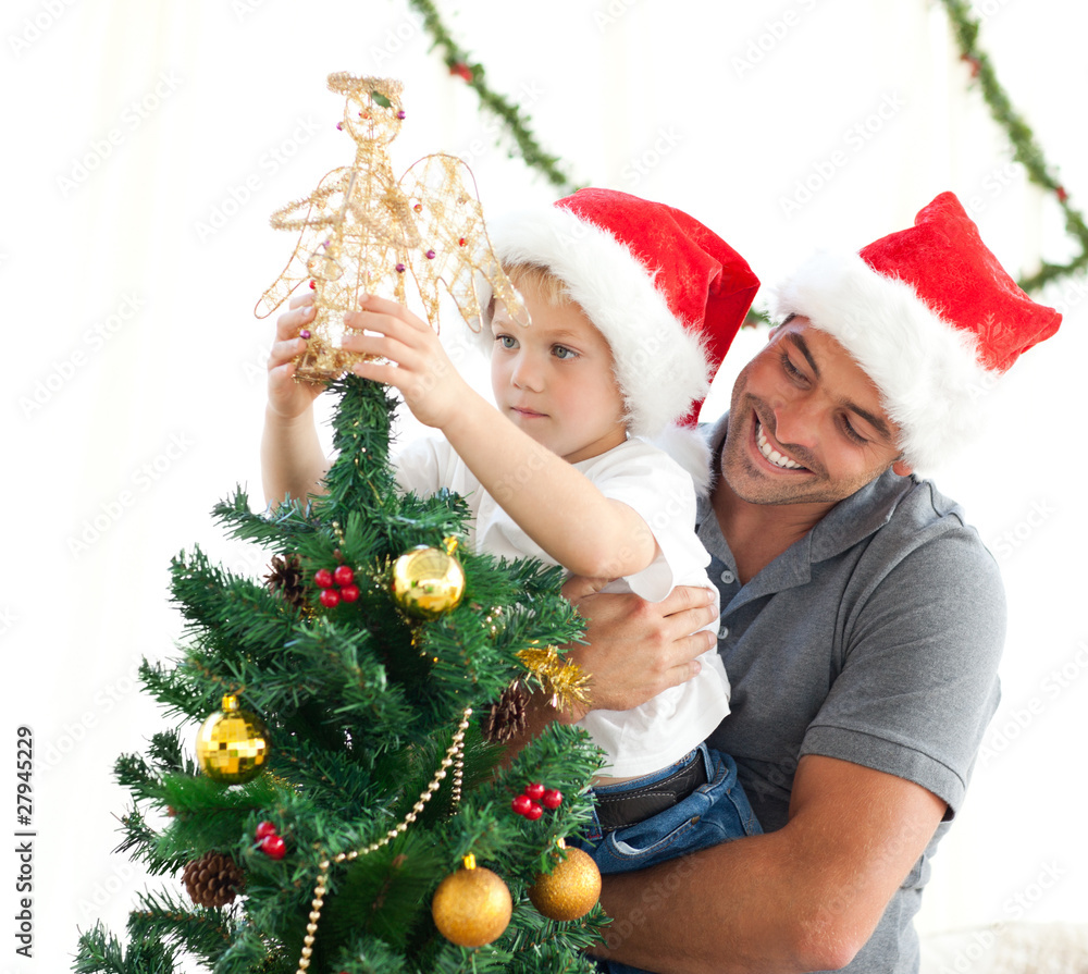 Father helping his son to put an angel on the Christmas tree Father helping his son to put an angel on the Christmas tree