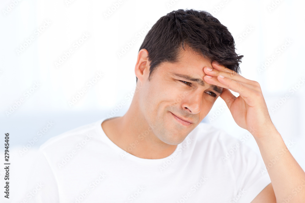 Worried man having a headache sitting in his bedroom Worried man having a headache sitting in his bedroom