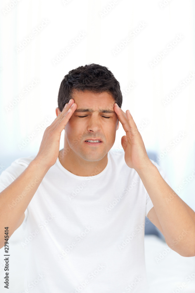 Man massaging his temples sitting on his bed Man massaging his temples sitting on his bed