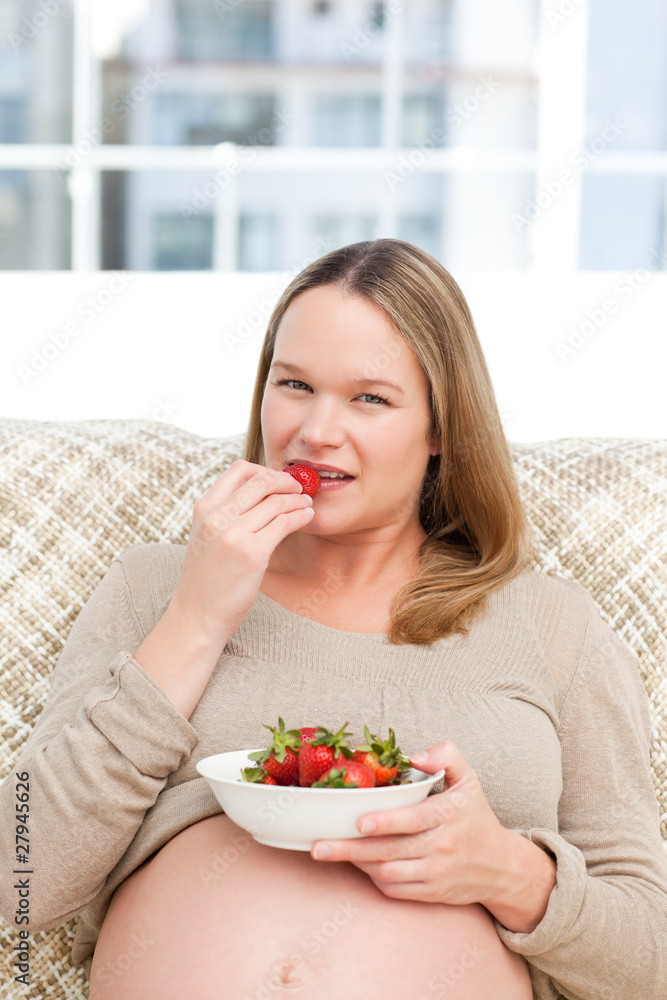 Serious future mom eating strawberries sitting on the sofa Serious future mom eating strawberries sitting on the sofa