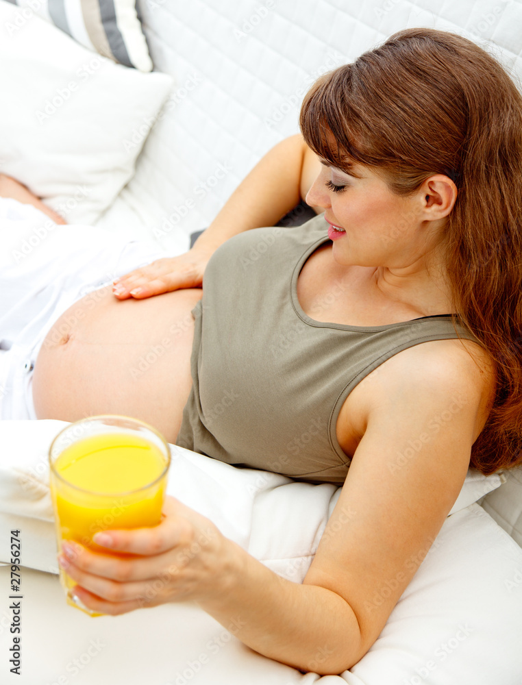 Beautiful pregnant female relaxing on sofa with glass of juice. Beautiful pregnant female relaxing on sofa with glass of juice.