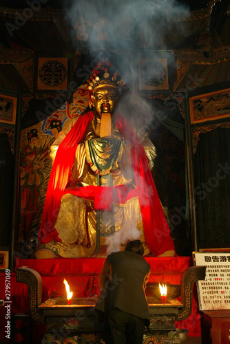 Woman making offering before a golden statue in Fengdu, China photo