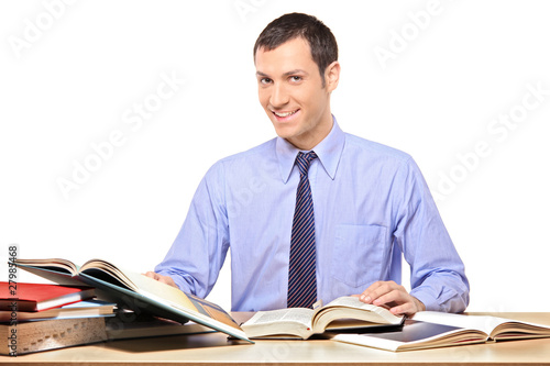 A man reading a book, with many other books on the desk photo