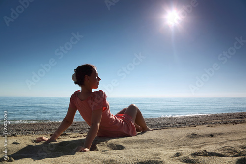 Woman in morning sits on sand leaning against hands near sea