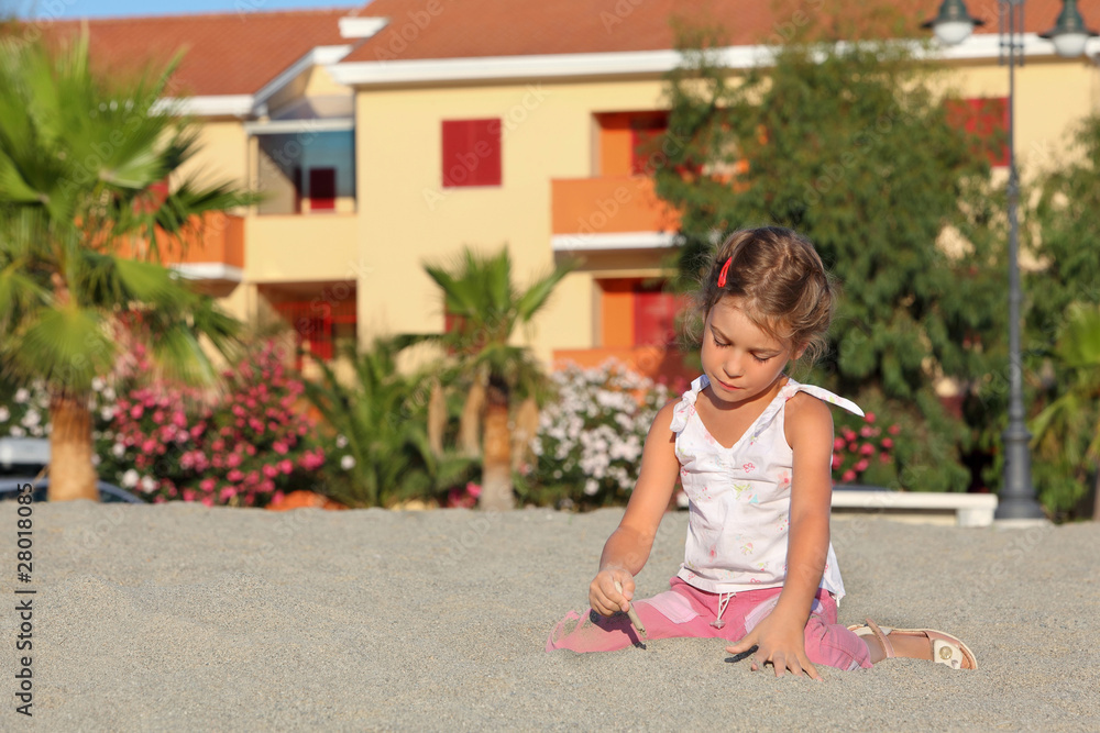 Girl sits in day-time on beach and interestedly leads stick Girl sits in day-time on beach and interestedly leads stick
