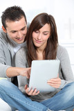 Young couple sitting on sofa with electronic pad