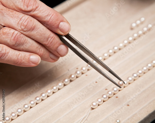 Close hand jeweler stringing pearls on a necklace