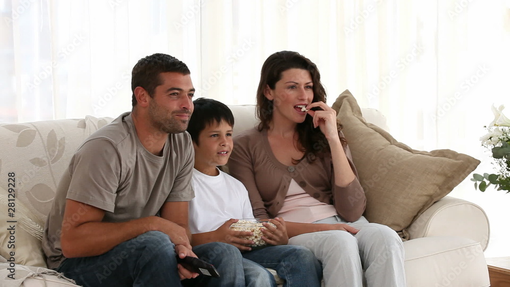 Happy family watching a movie and eating pop corn on the sofa Happy family watching a movie and eating pop corn on the sofa