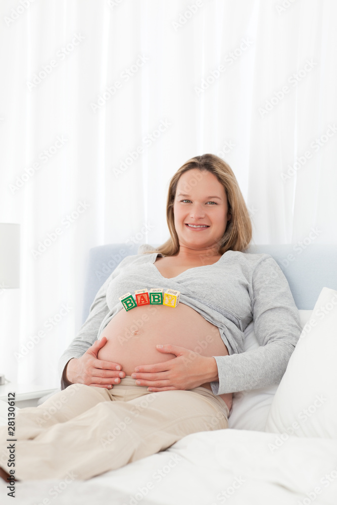 Adorable future mother with baby cubes on her belly on the bed Adorable future mother with baby cubes on her belly on the bed